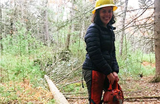 Emily Dolhansky in 2022, holding a saw next to a fallen tree