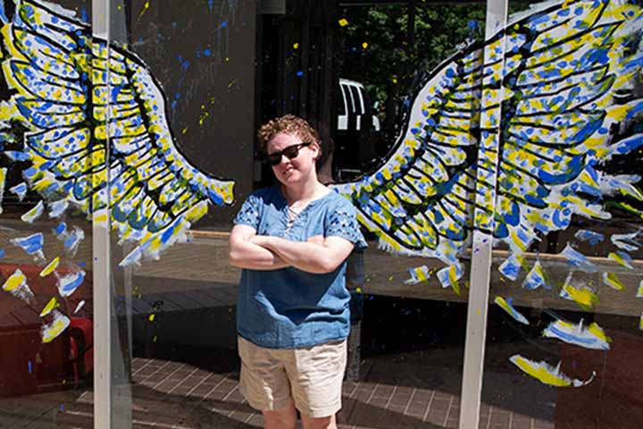 Loryn Stanton poses in between the blue and gold wings she painted on a window