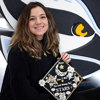 Angelina Maffei smiling and holding up her decorated cap for graduation