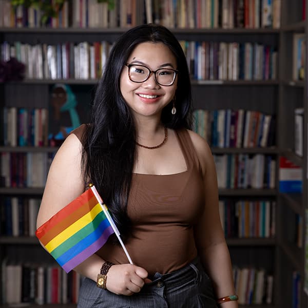 Van Nhi Ho holding up a pride flag in the Women's Gender & Sexuality Center's lounge