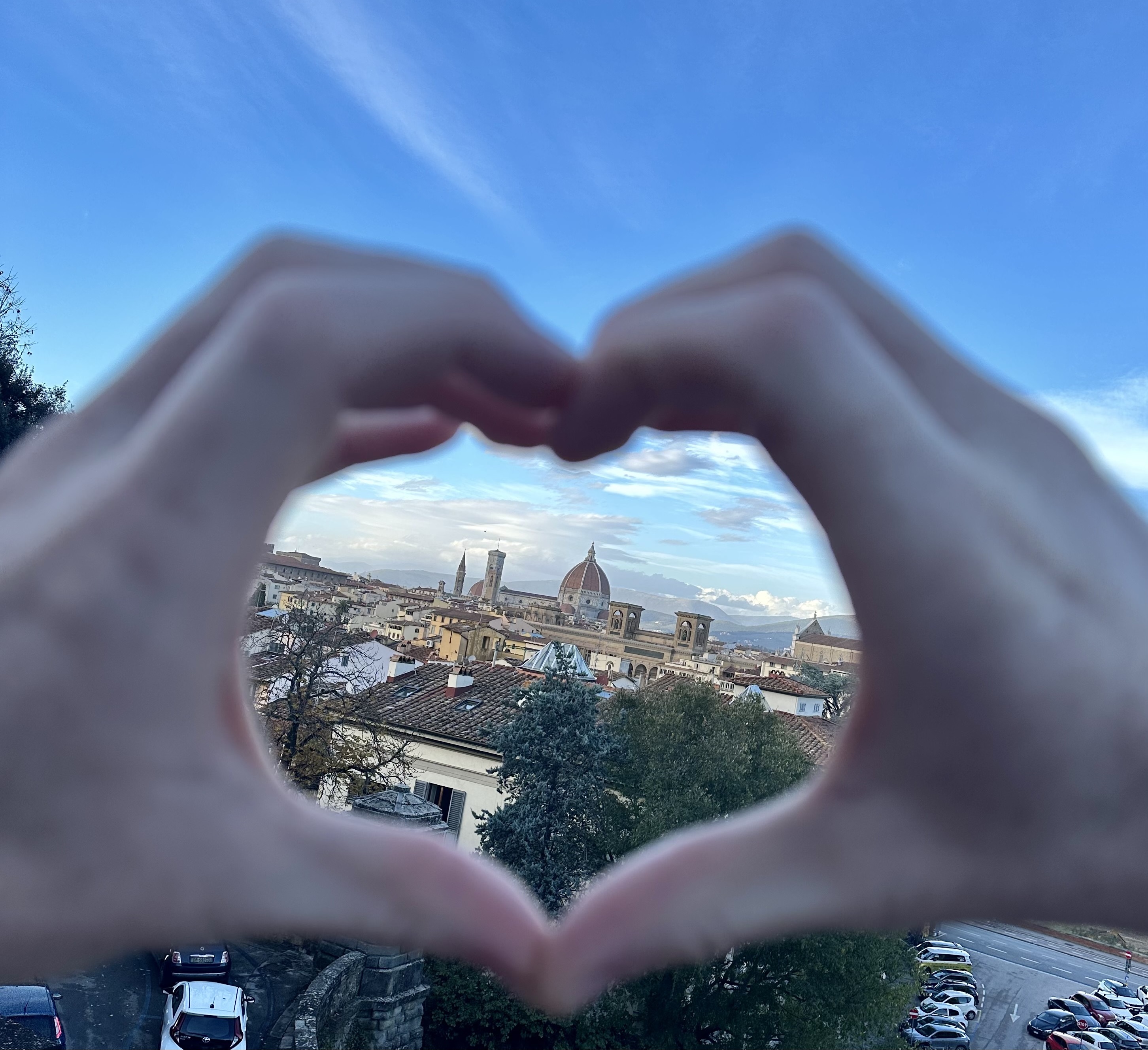 Two hands making a heart sign with the city of Florence, Italy inbetween the heart in the background.