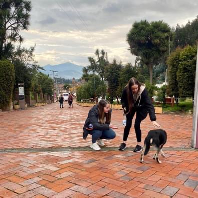 Two students outside leaning down to pet a dog in Colombia.