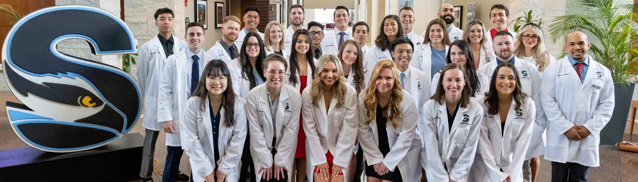 Doctor of Physical Therapy students in lab coats gather in a campus setting at Stockton University, representing hands-on clinical training and professional preparation.