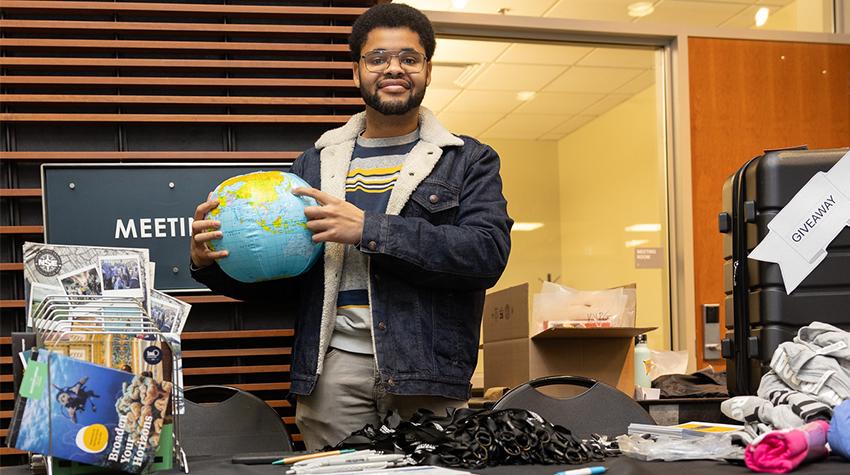 Student Avery Garlic holding a globe behind the Office of Global Engagement's table Student Avery Garlic holding a globe behind the Office of Global Engagement's table