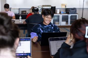 Lively lab session where students work on laptops and exchange ideas in Communication Studies.