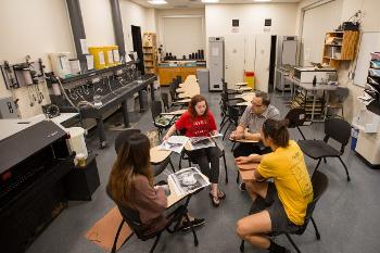 Visual Arts students gather in a small critique session, discussing photographic prints and developing their creative process.