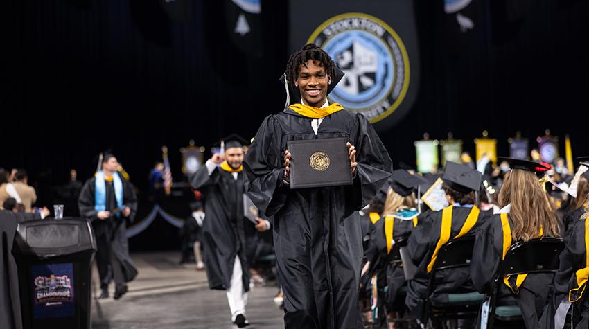 A graduate walking with their diploma A graduate walking with their diploma
