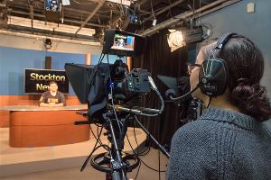 A Stockton University Communication Studies student films a live news segment in the campus television studio, gaining real-world broadcasting experience.