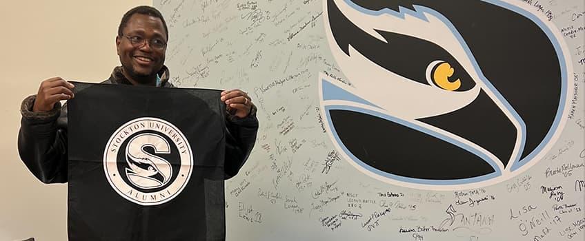 An alum holding up a Stockton University Alumni bandana after signing his name An alum holding up a Stockton University Alumni bandana after signing his name