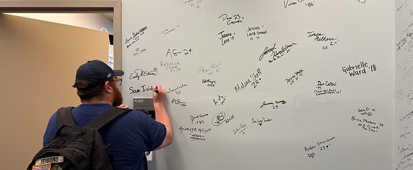 An alum signing their name on the Alumni Hall of Fame An alum signing their name on the Alumni Hall of Fame