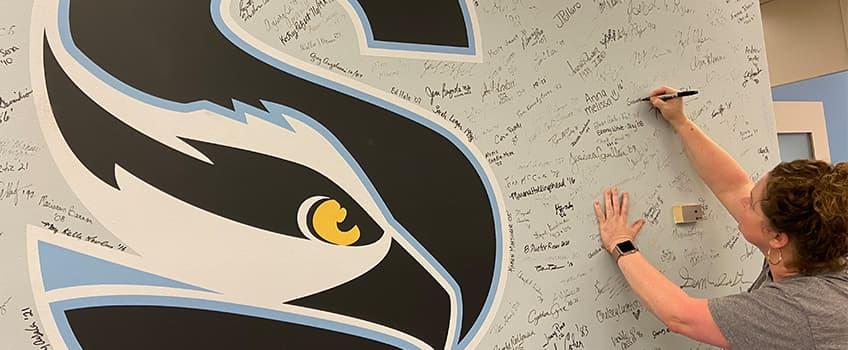 An alum signing their name on the Alumni Hall of Fame An alum signing their name on the Alumni Hall of Fame