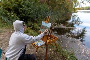 A student paints outdoors by Lake Fred, finding inspiration in Stockton’s natural surroundings and tranquil landscapes.