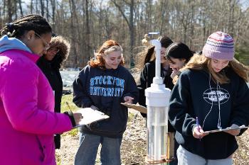 Students collect and record environmental data in the field using scientific monitoring equipment.