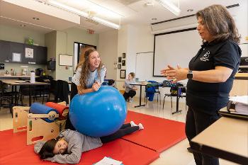 An occupational therapy faculty member guides students through a hands-on lab activity using therapeutic equipment, demonstrating the collaborative learning and individualized instruction built into the Stockton MSOT experience.