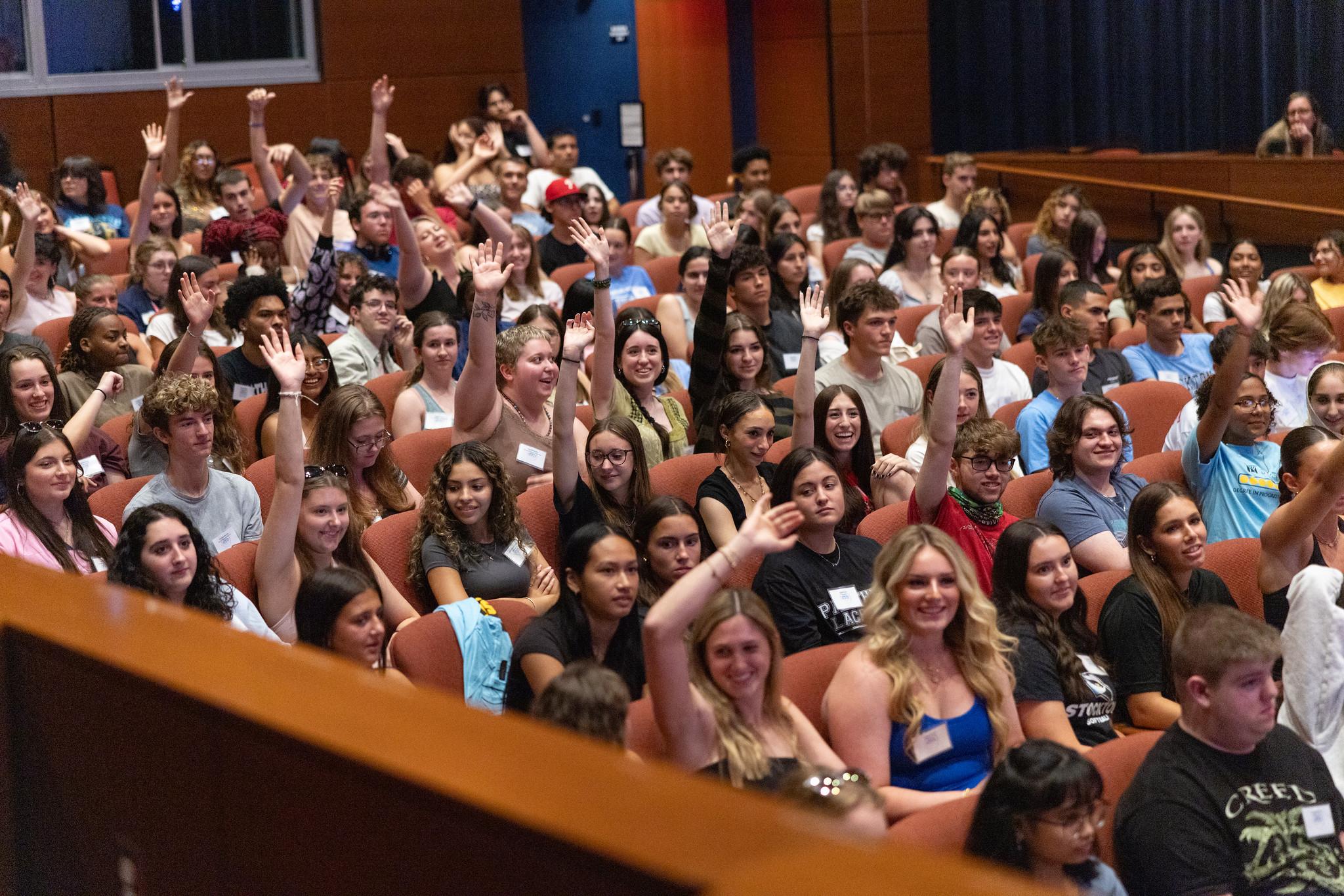 students smiling and raising their hands engaging in an orientation session held in the Campus Center theater