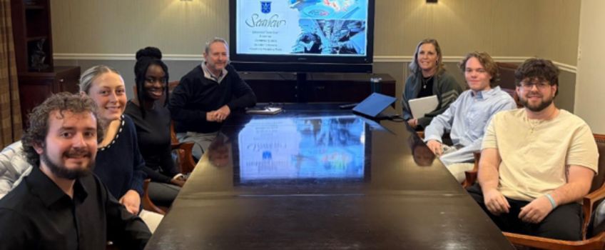 Students of Michael Scales meet with Mike Tidwell, Director of Sales & Marketing at Seaview Hotel. The group sits around a conference table and smiles toward the camera. 
