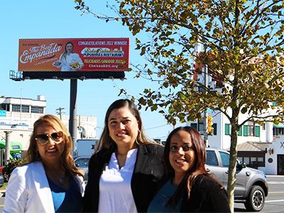 Ana Salazar (center) and Yoely Quezada (right) under Salazar's new billboard. Salazar's restaurant won a "Best Empanada" contest.