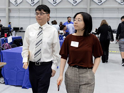 Students Andy Vuong and Bianca Hernandez walking past tables.