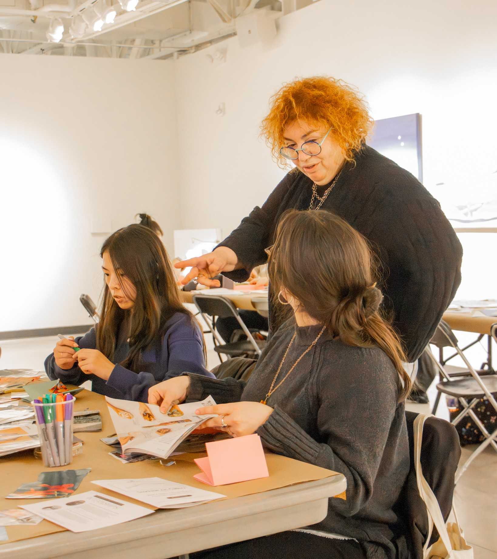 Fulbright Scholar Desislava Hristova-Tosheva works with two students at a table during a zine and collage workshop in an art gallery classroom.