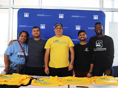 Members of Student Development and SCCESL posing and smiling behind a table of free t-shirts.