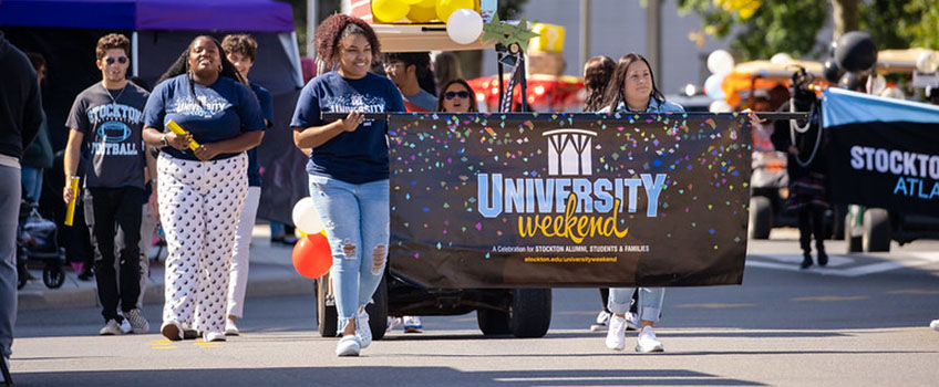 Students walk in the Street Fair with a University Weekend banner.