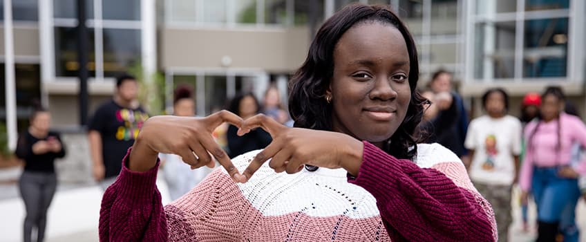 A student making a heart with her hands in front of the Multicultural Center
