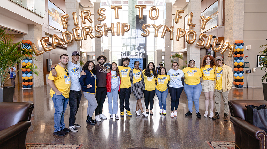 First to Fly leadership team in front of the balloon banner in the Campus Center