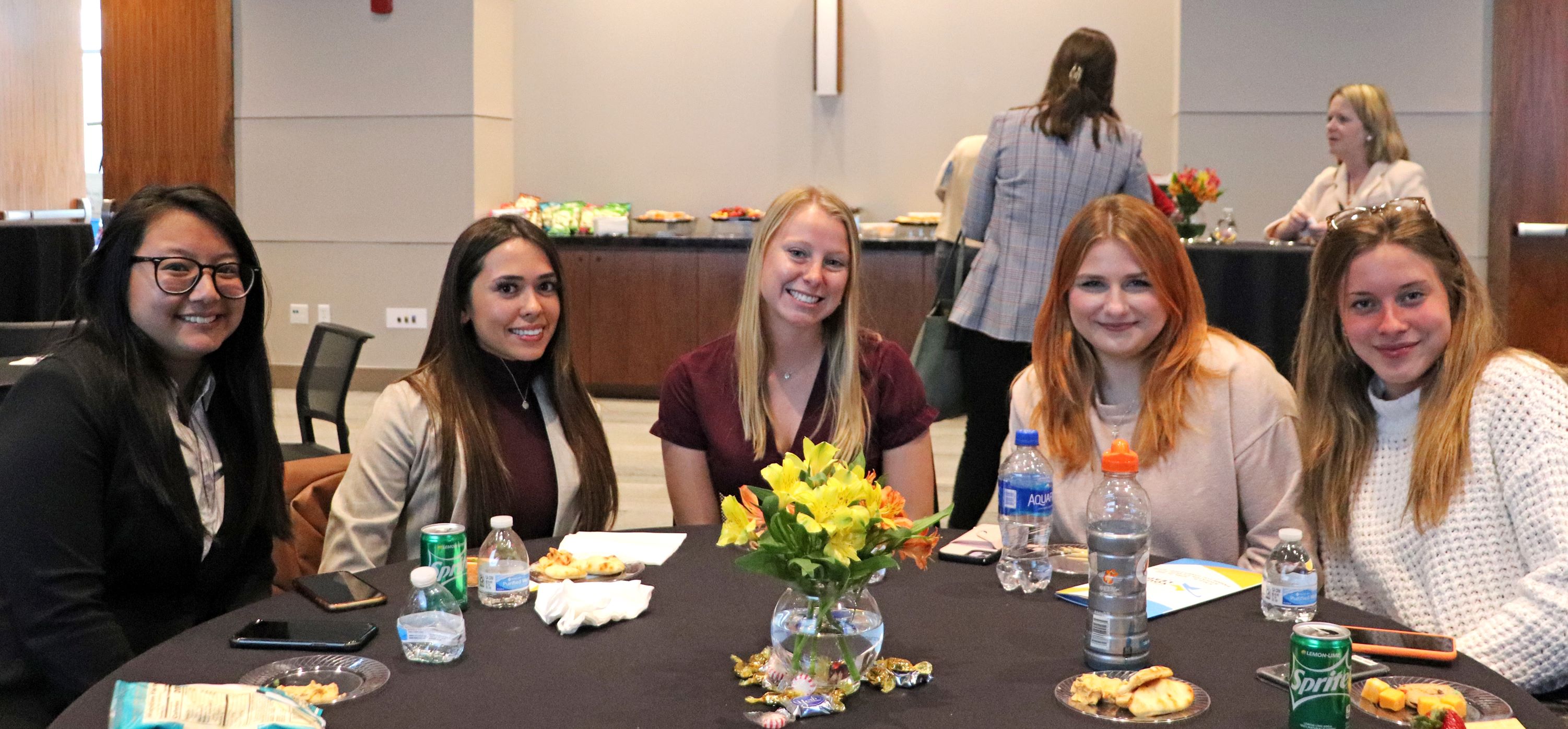 Several students from the 3230 Event Experience class involved with organizing the Young Leaders Expo sit at a table and smile for the camera.
