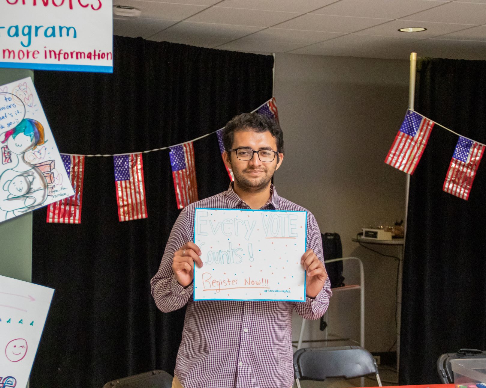 A student holds up a poster that reads, "Every vote counts!! Register Now!!"