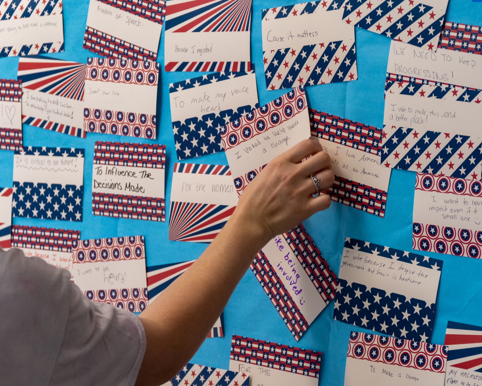 A student tapes a piece of paper on the "Why I'm Voting Wall," which is adorned with reasons why students vote.