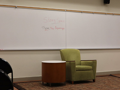 A green chair in front of a white board that says "Story Space, Theme: New Beginnings." This chair will be where students share their stories.