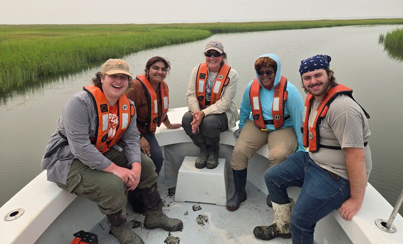 Students in a boat on the Mullica River with instructor of Biology Melanie Schroer
