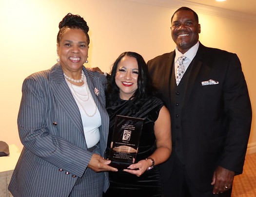 two women holding award and man standing to their right