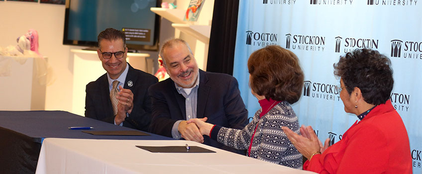  President Bertolino and Pam Monaco, president of OCC, celebrate after signing a 3+1 transfer agreement for Hospitality Studies students Dec. 16. Stockton Provost and Vice President for Academic Affairs Michael Palladino, left, and Eileen Garcia, vice president of Academic Affairs at OCC, look on.