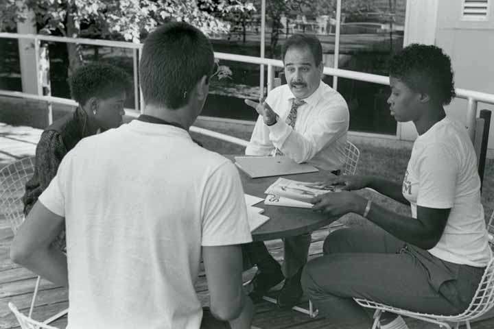 A black and white image of Harvey Kesselman seated at a round table with students