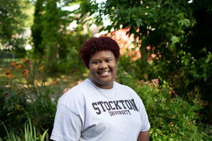 Damaris-Anne Spring wears a Stockton t-shirt surrounded by the natural foilage of campus