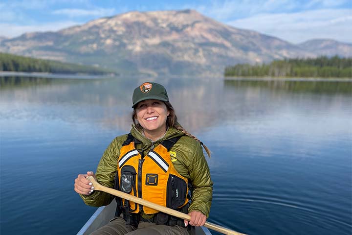 Kimberly Dudeck holds an oar sitting in a canoe with a mountain behind her