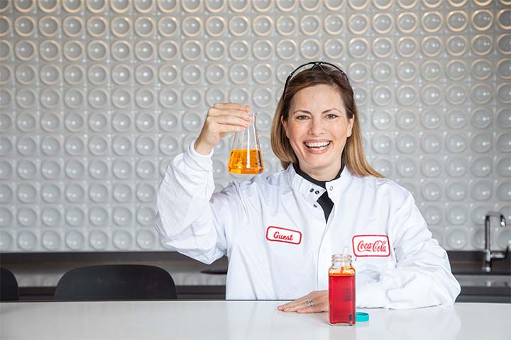 Cathianne Leonardi wears a white lab coat and holds a beaker filled with an orange substance