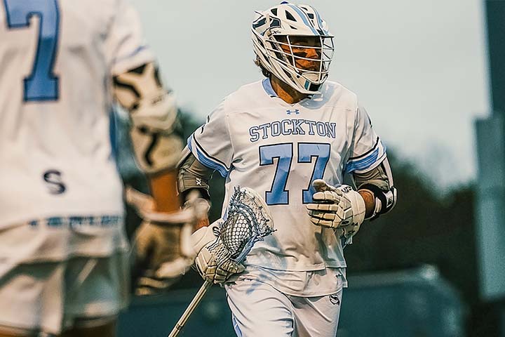 Luc Swedlund in his white and blue lacrosse uniform with helmet and lacrosse stick