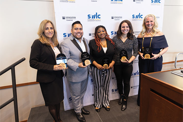 One male and four female award winners stand and pose with their Excellence in Mentoring awards