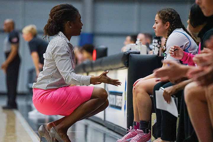 Devin Jefferson in pink skirt kneels in front of her players to offer wisdom during a basketball game