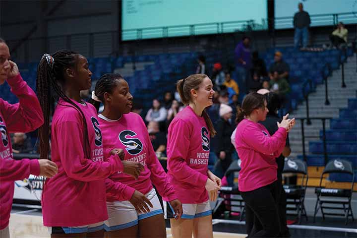 A few women's basketball players wearing bright pink warm-up shirts before a game