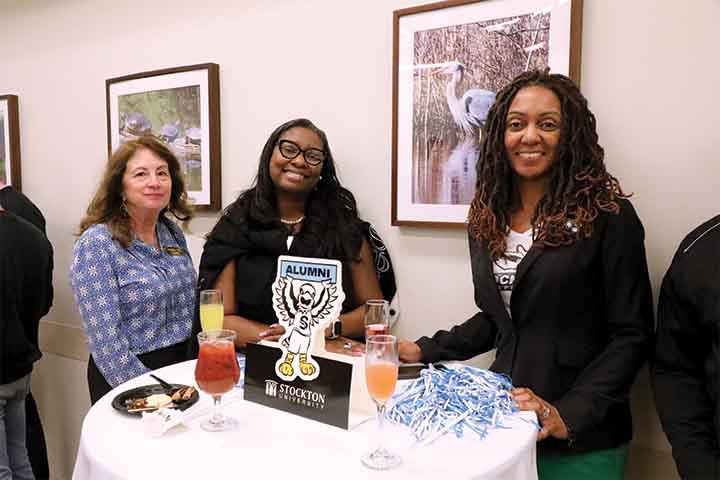 Three female alumni stand at a cocktail table in the Campus Center