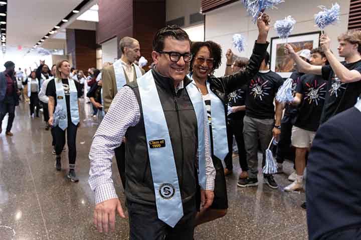 Brian Nelson wearing a blue Stockton stole with a Class of 1999 badge