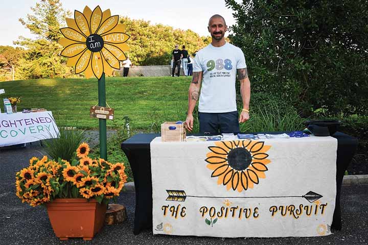 Jared Lombardi standing behind a table promoting The Positive Pursuit with sunflowers
