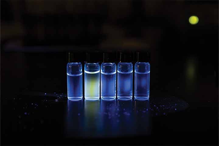 The second of five small vials glows bright yellow-green under a black light 