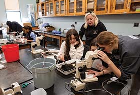 High school students examine sea grass through a microscope while their teacher looks on