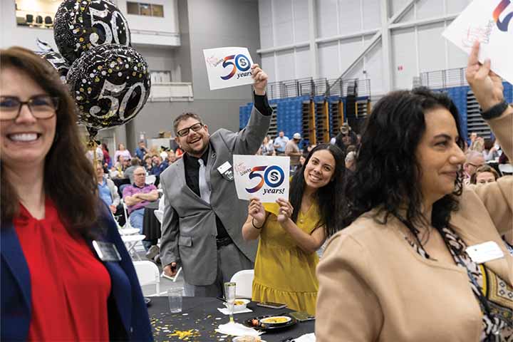 Demetrios Roubos and Jessica Cruz-Irwin hold small signs with "50 Years" inside the Sports Center