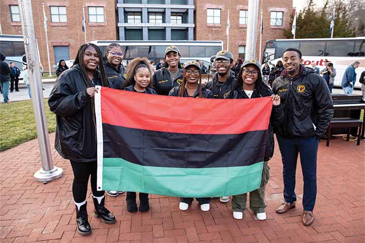 A group of students and staff hold the Pan African flag with red, black and green stripes outside the Arts and Sciences Building