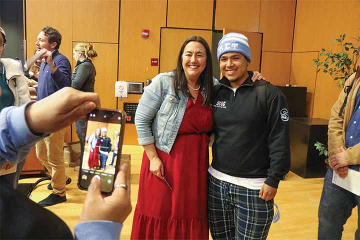 Erin Gruwell in red dress and denim jacket smiles with a student with blue hat and black shirt